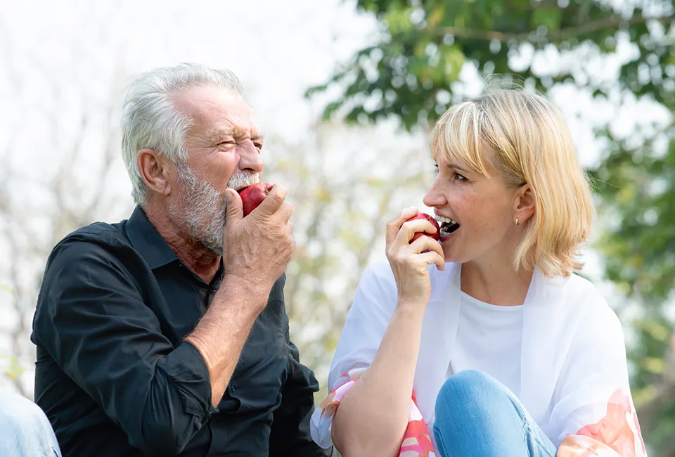 Happy patient biting apple with dental implants in West Hollywood, CA